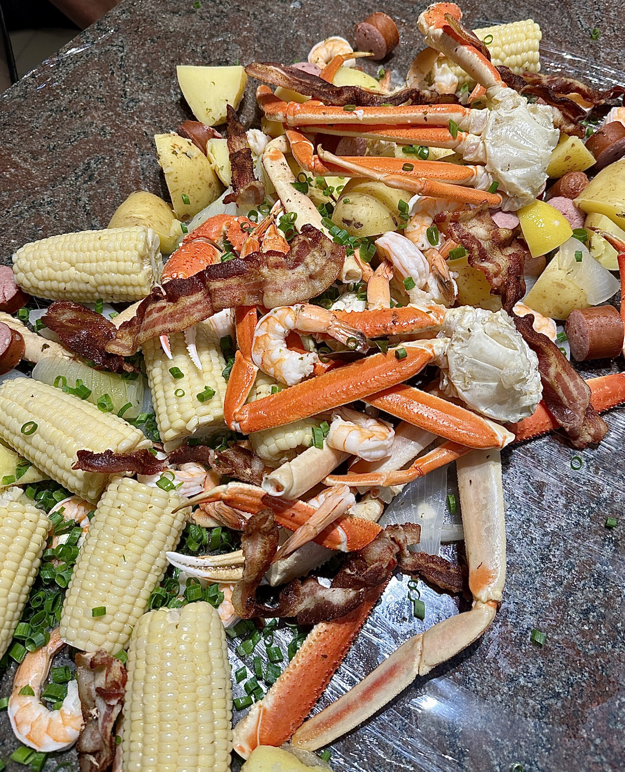 Vibrant seafood boil spread with snow crab, shrimp, andouille sausage, corn, and potatoes, seasoned with spices and herbs, served on a table.